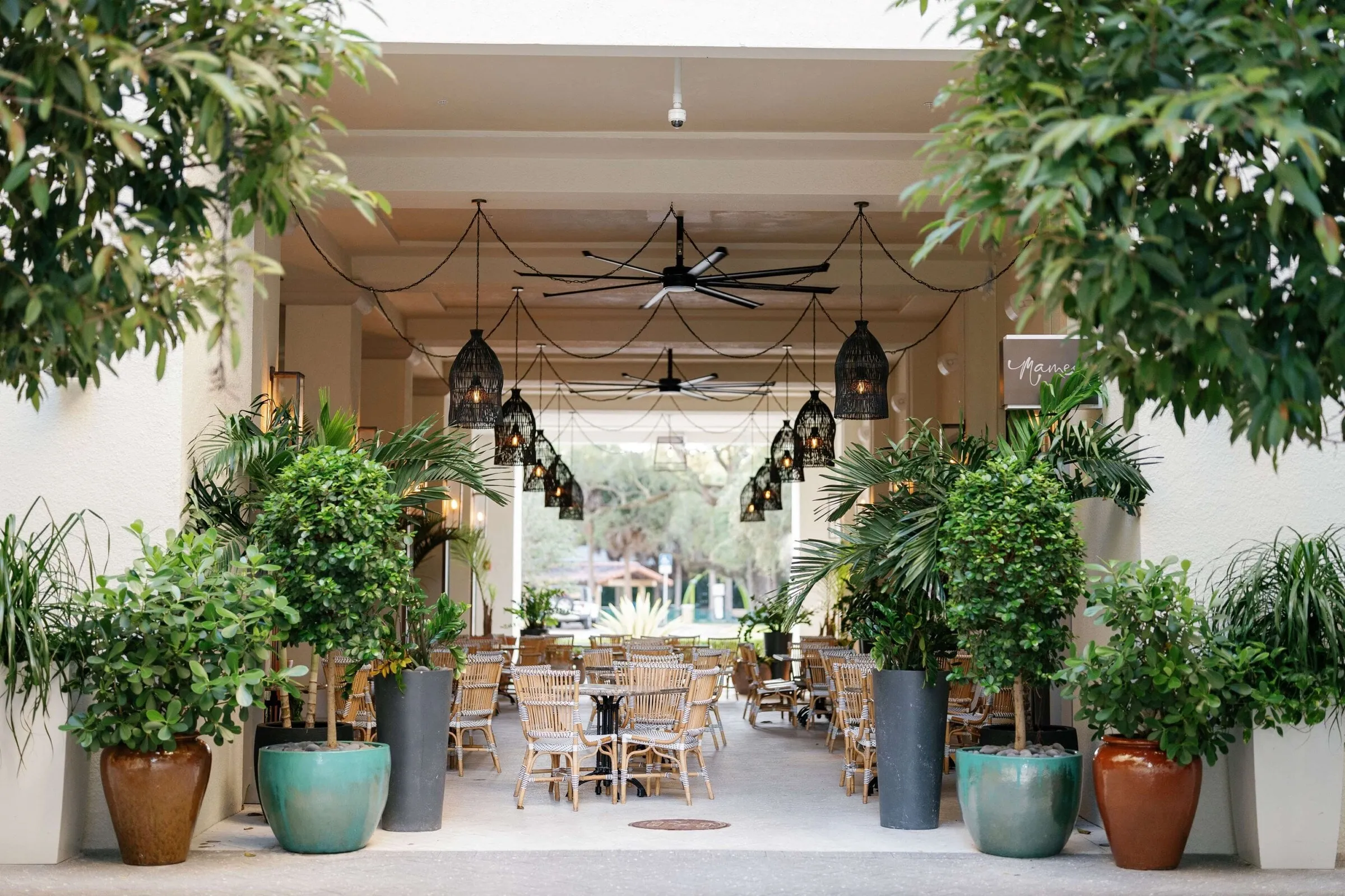 The covered terrace at Thesis Hotel, with hanging rattan lanterns, potted palms and rows of bistro chairs