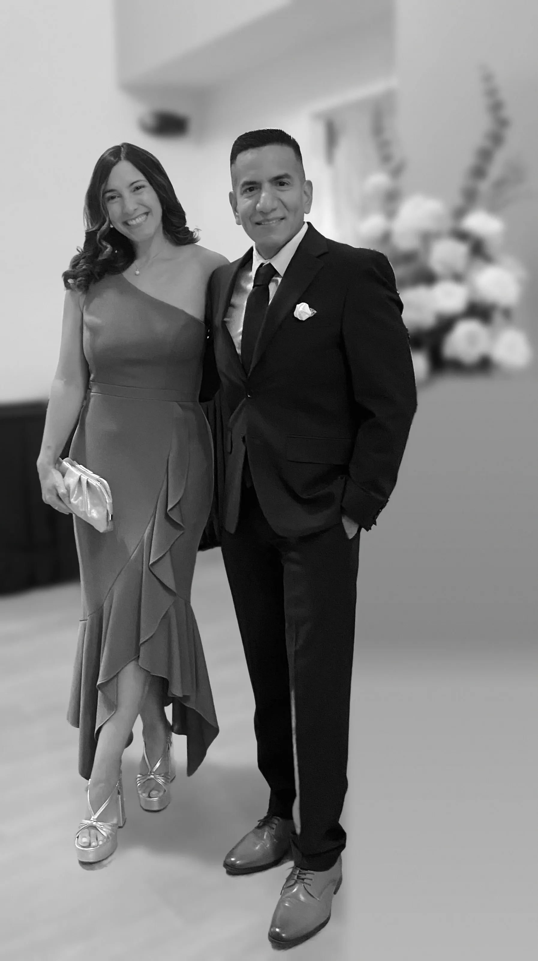 Katherine in a one-shoulder ruffled gown and Isaac in a dark suit, smiling side by side